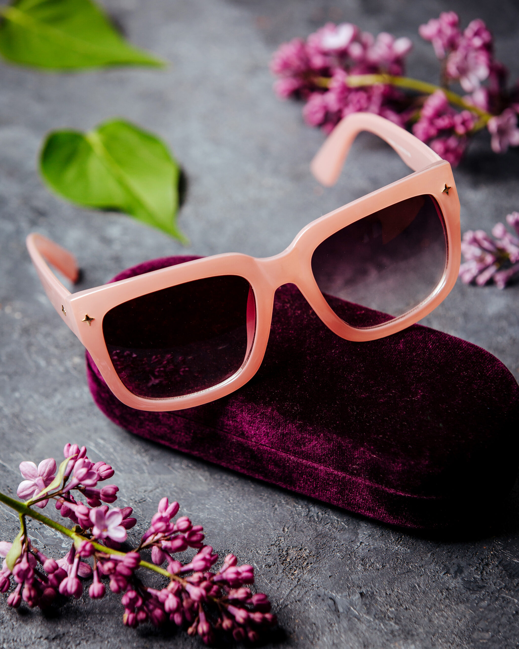 pink-sunglasses-around-beatiful-flowers-grey-surface
